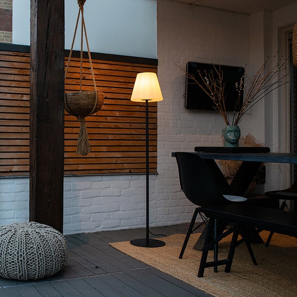 Modern gestaltete Terrasse mit einer Stehleuchte, einem Esstisch mit Stühlen, einem Hängekorb an einem Holzbalken und einem geflochtenen Pouf.