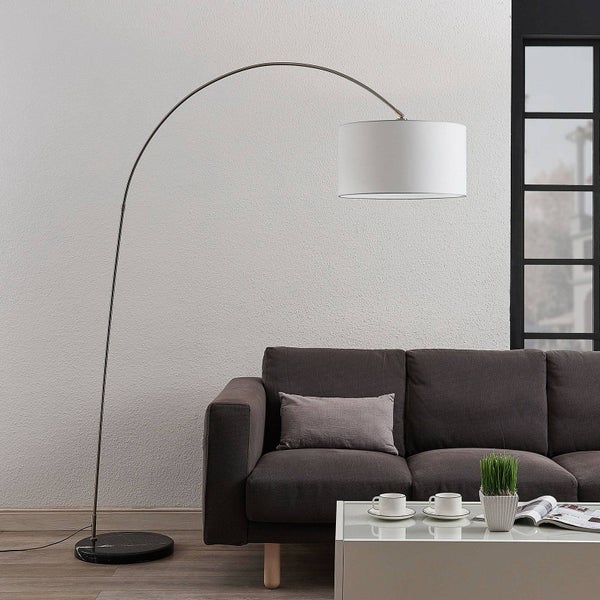 Moderne Bogenstehlampe mit weißem Stoffschirm und schwarzem Marmorfuß in einem Wohnzimmer mit dunkelgrauem Sofa.