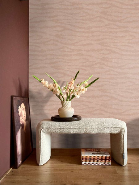Wohnzimmer mit Vliestapete mit Wellenmuster an der Wand, dazu eine Sitzbank aus Boucle-Stoff, eine Vase mit Blumen und ein gerahmtes Bild.