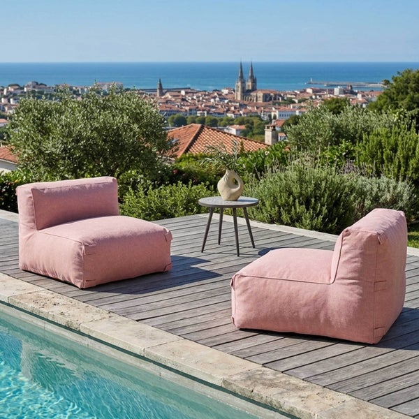 Zwei rosafarbene Outdoor-Sitzsäcke auf einer Holzterrasse am Pool, kleiner Beistelltisch, im Hintergrund Stadtpanorama am Meer.