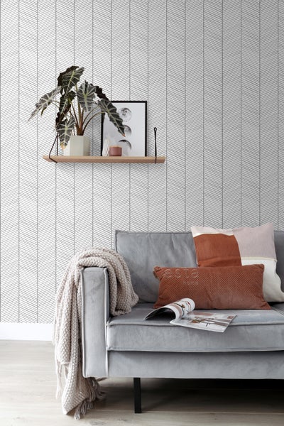 Wohnzimmer mit gemusterter Tapete, Sofa, Kissen, Decke und Regal mit Dekoration