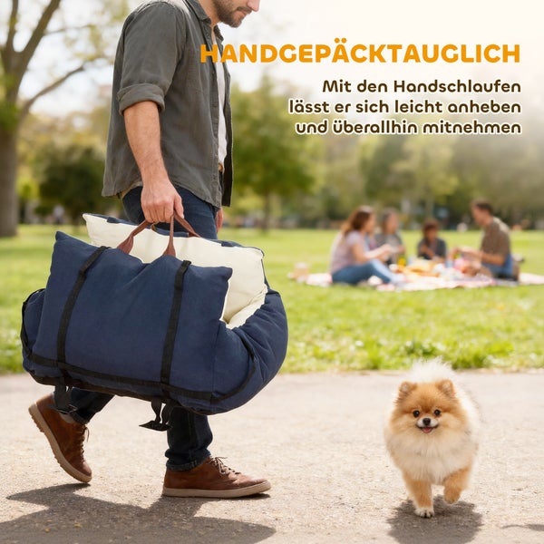 Tragbares Hundereisebett mit Handschlaufen, getragen von einem Mann in einem Park neben einem kleinen Hund.