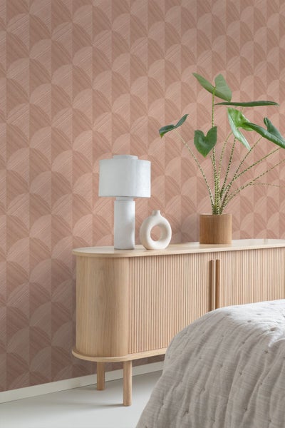 Tapete mit geometrischem Fächermuster hinter einem hellen Sideboard aus Holz mit Lamellen, einer weißen Lampe und einer Zimmerpflanze.