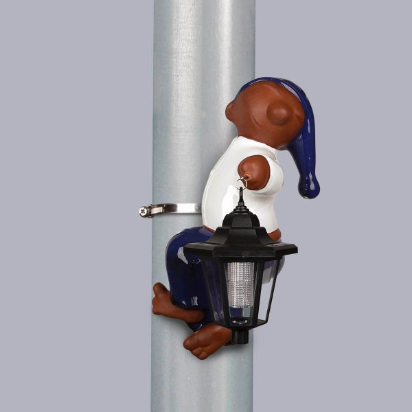 Sandmännchen-Gartenfigur mit Solarlaterne, mit einer Metallschelle an einem Mast befestigt.