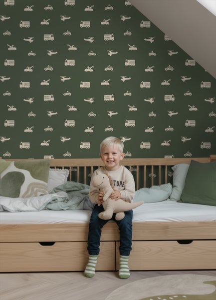 Vliestapete im Kinderzimmer mit Fahrzeug-Motiven auf dunkelgrünem Hintergrund, kombiniert mit einem hellen Holzbett in einer modernen Einrichtung.