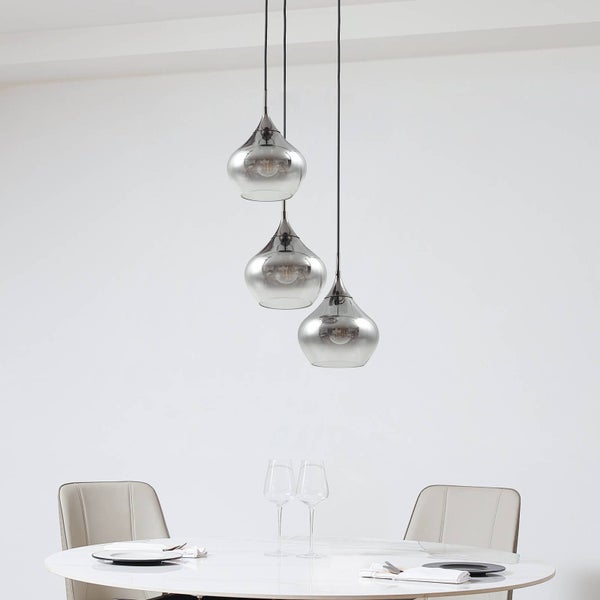 Moderne dreiflammige Pendelleuchte mit getönten Glasschirmen über einem weißen runden Tisch in einem hellen, organisierten Essbereich.