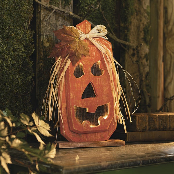 Dekorative Kürbisfigur aus Holz mit gruseligen Gesichtszügen und Strohhaaren für Halloween.