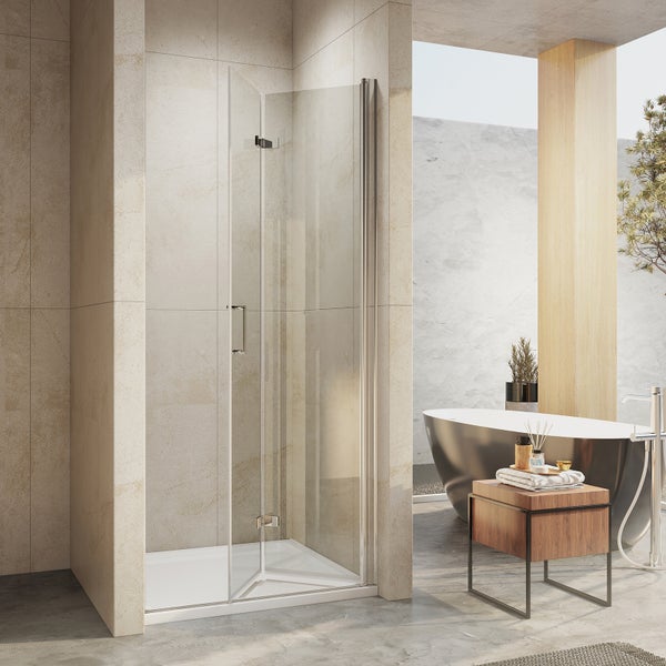 Rahmenlose Duschkabine aus Klarglas mit Metallelementen in einem hellen Badezimmer mit Badewanne und Steinfliesen.