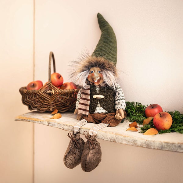 Dekorative Elfenfigur auf einem Regal mit Äpfeln im Korb und losen Äpfeln