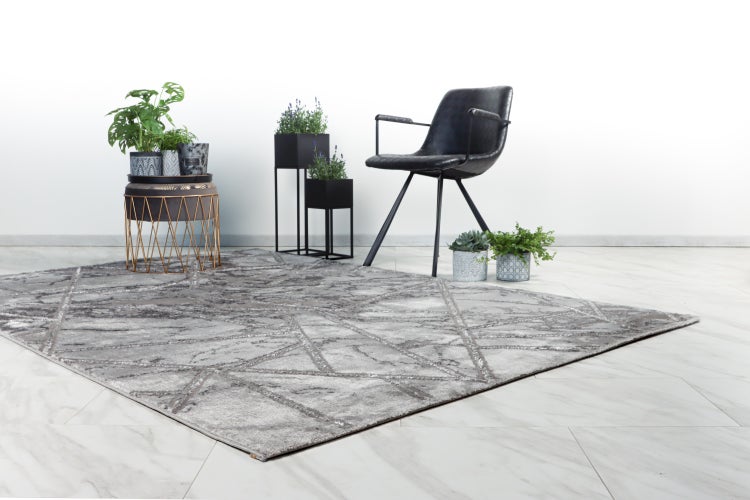 Grauer moderner Teppich mit geometrischem Muster in einem stilvoll eingerichteten Wohnbereich mit Sessel und Pflanzen.