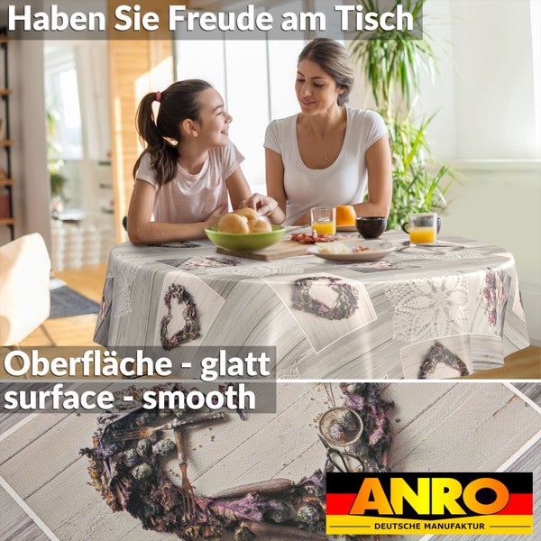 Runde, glatte Wachstischdecke mit Holzoptik und Blumenkranz-Motiv auf einem gedeckten Frühstückstisch in einem hellen Raum.