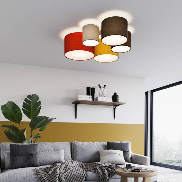 Moderne Deckenleuchte mit fünf zylindrischen Textilschirmen in verschiedenen Farben über einem grauen Sofa in einem hellen Wohnzimmer.
