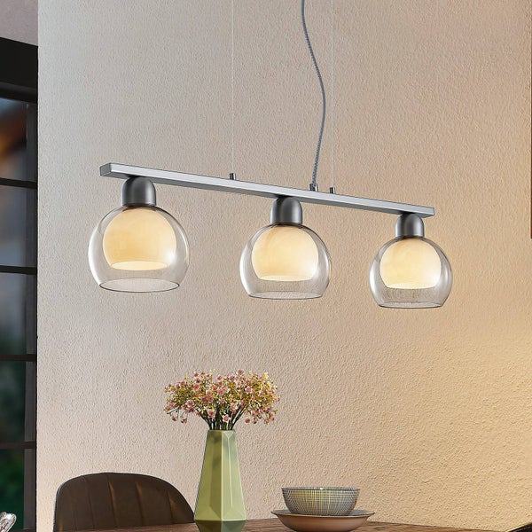 Pendelleuchte mit drei Lampen aus Glas und Metall über einem Esstisch.