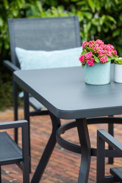 Organisierte Sitzgruppe mit einem modernen Metall-Gartentisch und Gartenstühlen mit Armlehnen auf einer hellen Terrasse mit Pflanzen.