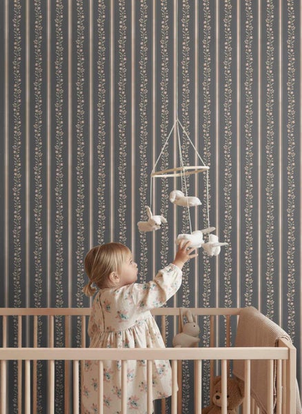 Gestreifte Tapete mit floralem Rankenmuster in einem Kinderzimmer hinter einem Gitterbett mit einem Kind.