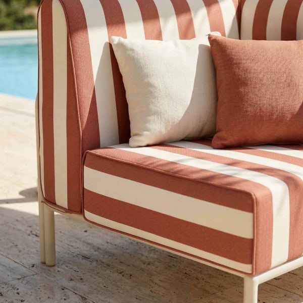 Gestreiftes Outdoor-Sofa mit zwei Dekokissen auf einer Terrasse an einem Pool.