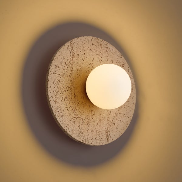 Moderne Wandleuchte mit runder, texturierter Basis aus Steinoptik und einer mittigen, leuchtenden Glaskugel.