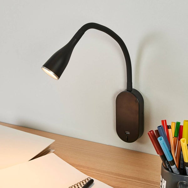 Schwarze flexible LED-Leseleuchte mit USB-Anschluss montiert an der Wand über einem Schreibtisch mit Notizbuch und Stiften.