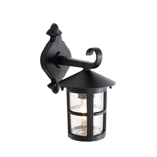 Klassische Außenwandleuchte aus schwarzem Metall im Laternendesign mit strukturiertem Glas und eingeschalteter Lichtquelle.