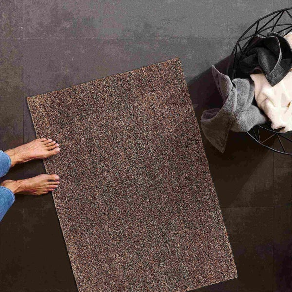 Fußmatte aus Textilgewebe auf Bodenfliesen neben einem Wäschekorb mit Textilien