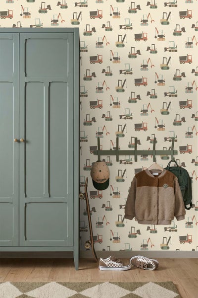Wand im Kinderzimmer mit Tapete mit Baustellenfahrzeug-Motiv, daneben ein Kleiderschrank, eine Hakenleiste mit Kleidung und ein Skateboard.