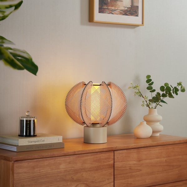 Moderne Tischlampe mit gewelltem Schirm aus Holzlamellen auf einer Holzkommode mit Dekoration.