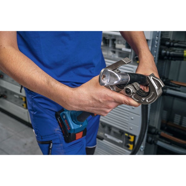 Eine Person hält eine elektrische Crimpzange in den Händen. Eine Bosch-Bohrmaschine befindet sich am Gürtel der Person.