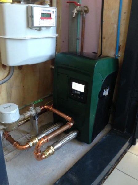 Installierte DAB Wasserpumpe in Grün und Schwarz mit Digitalanzeige, angeschlossen an Kupferrohre und flexible Schläuche.