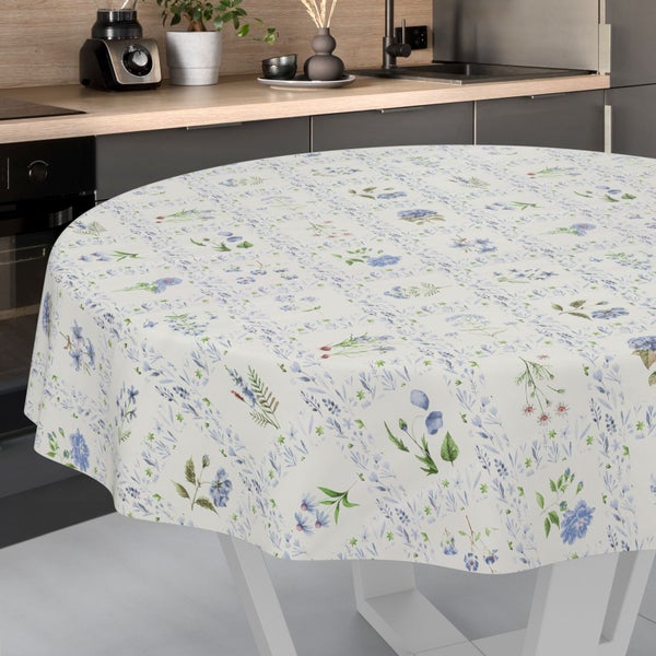 Runde Tischdecke mit floralem Muster aus blauen Blumen und grünen Blättern auf einem weißen Tisch in einer modernen Küche.