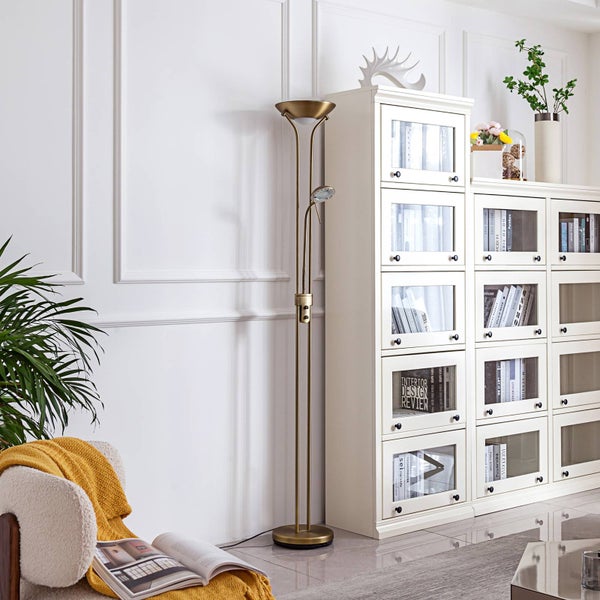 Klassische Stehleuchte aus Messing mit Deckenfluter und verstellbarem Lesearm in einem hellen Wohnzimmer neben einem weißen Bücherregal.