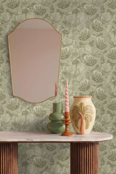 Wohnraum mit floraler Tapete, einem geschwungenen Wandspiegel, einer Vase mit Palmenmotiv, einer grünen Vase und einer gedrehten Kerze auf Konsole.