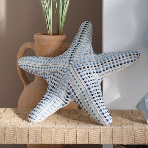 Dekoratives Kissen in Seesternform mit blau-schwarzem Muster auf einer geflochtenen Bank neben einer Terrakottavase.