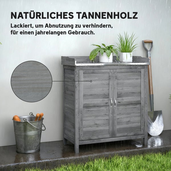 Gartenschrank aus grau lackiertem Tannenholz mit zwei Türen, Arbeitsplatte und Pflanzen im Regen neben Eimer und Spaten.