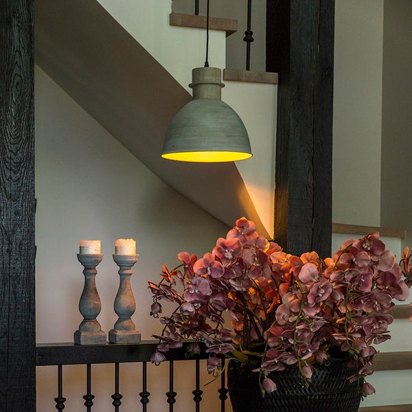 Graue Pendelleuchte im Industriestil über einer Treppe mit zwei Kerzenständern und einem Korb mit rosa Orchideen.