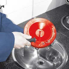 Eine Person benutzt ein Rothenberger Rohrreinigungsgerät zum Reinigen des Abflusses in einem Edelstahlwaschbecken.