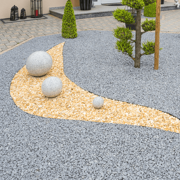 Modern gestaltetes Gartenbeet mit Zierkies, drei Granitkugeln unterschiedlicher Größe und einem Formgehölz in einer gepflegten Außenanlage.