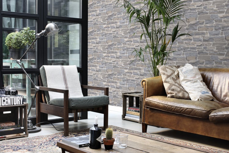 Wohnzimmer mit Steintapete, Sessel, Ledersofa und dekorativen Elementen für eine gemütliche Atmosphäre.