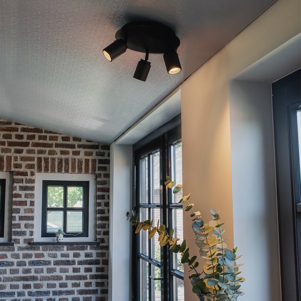 Deckenleuchte mit drei Strahlern in einem Raum mit Backsteinmauer und Fenstern