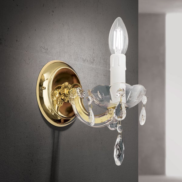 Klassische Wandleuchte in Kerzenoptik mit Kristallbehang und goldfarbener Wandhalterung an einer dunklen Wand.