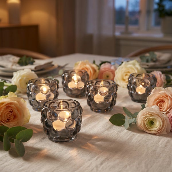 Festlich gedeckter Tisch mit fünf strukturierten Teelichthaltern aus Glas und frischen Blumenarrangements aus Rosen und Eukalyptus.
