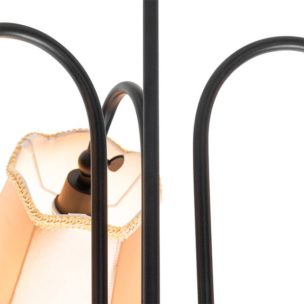 Detailansicht einer Lampe mit geschwungenen schwarzen Metallarmen und hellem Textilschirm mit dekorativem Rand.