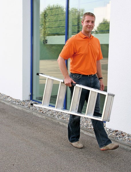 Ein Mitarbeiter trägt eine zusammengeklappte Aluminium Mehrzweckleiter im Außenbereich eines Hornbach Marktes.