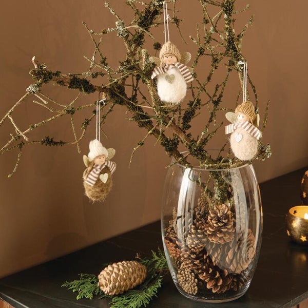 Drei hängende Weihnachtsengel aus Filz und Strick in einer mit Tannenzapfen gefüllten Glasvase auf einem Zweig als weihnachtliche Tischdekoration.