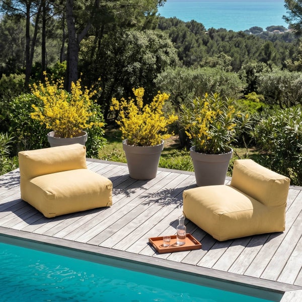 Zwei gelbe Outdoor-Sessel auf einer Holzterrasse am Pool. Drei graue Pflanzkübel mit gelben Blumen stehen im Hintergrund.