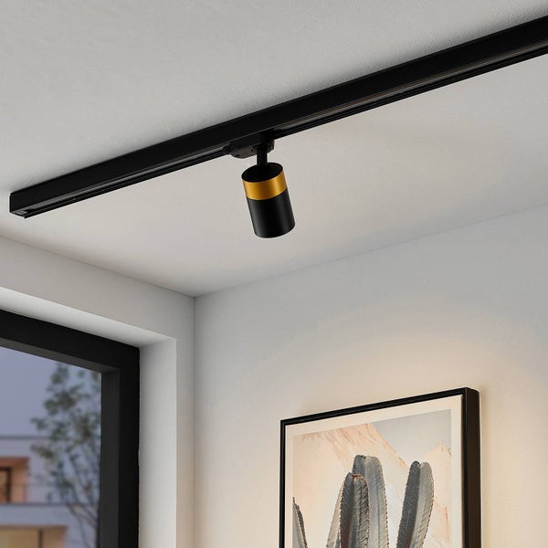 Schwarzes Schienensystem mit einem zylindrischen Strahler in Schwarz und Gold an einer weißen Decke.