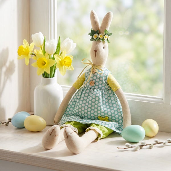 Stoffosterhase mit Kleid und Blumenkranz auf Fensterbank mit Osterdeko, Narzissen und Tulpen in Vase und Ostereiern.