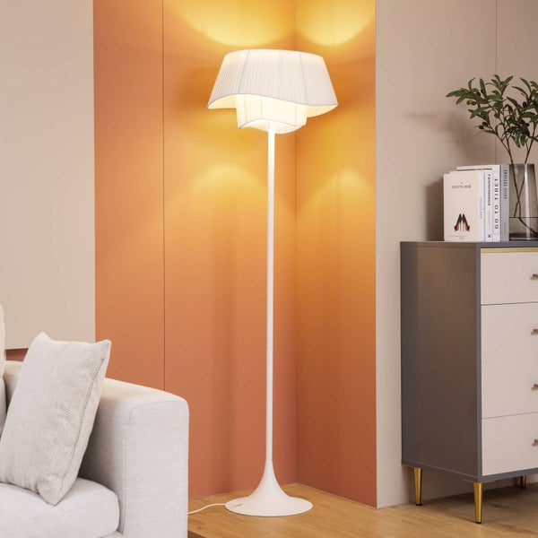 Stehlampe mit weißem, plissiertem Lampenschirm in einem Wohnzimmer.