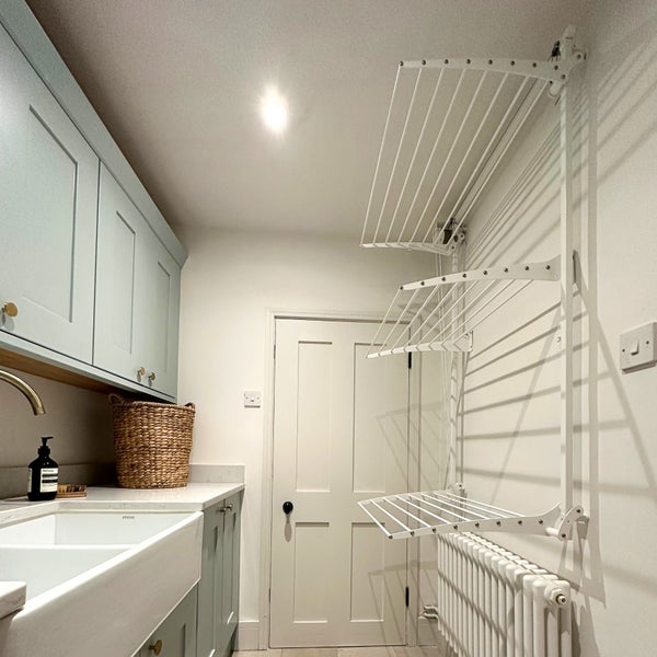 Heller Hauswirtschaftsraum mit Waschbecken, Schränken und einem an der Wand montierten Wäscheständer.