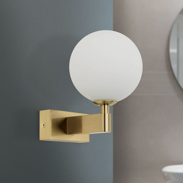 Moderne Wandleuchte in Messingoptik mit kugelförmigem Glaskopf montiert an einer Wand