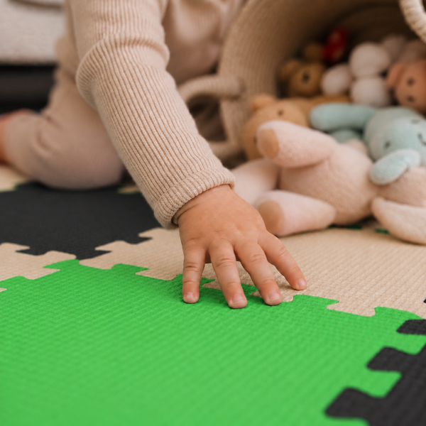 Kind spielt auf einer gepolsterten Spielmatte mit ineinandergreifenden Puzzleteilen und Stofftieren im Korb.
